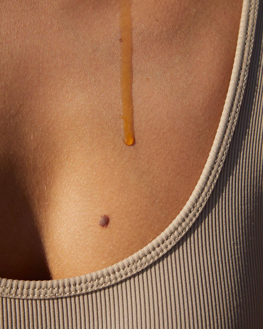 Torso of a person with tan skin wearing a ribbed tank top with a stream of honey or liquid dripping down the chest.