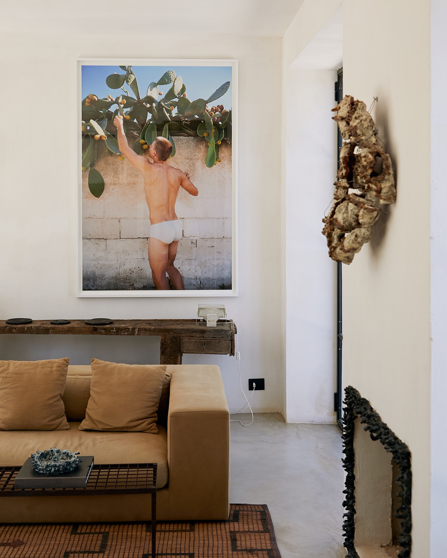 Interior view featuring a tan sofa, rustic console table, and a framed art print of a man reaching for fruit in an indoor space.