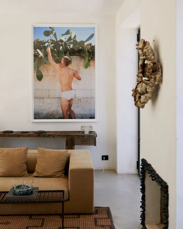 Interior view featuring a tan sofa, rustic console table, and a framed art print of a man reaching for fruit in an indoor space.