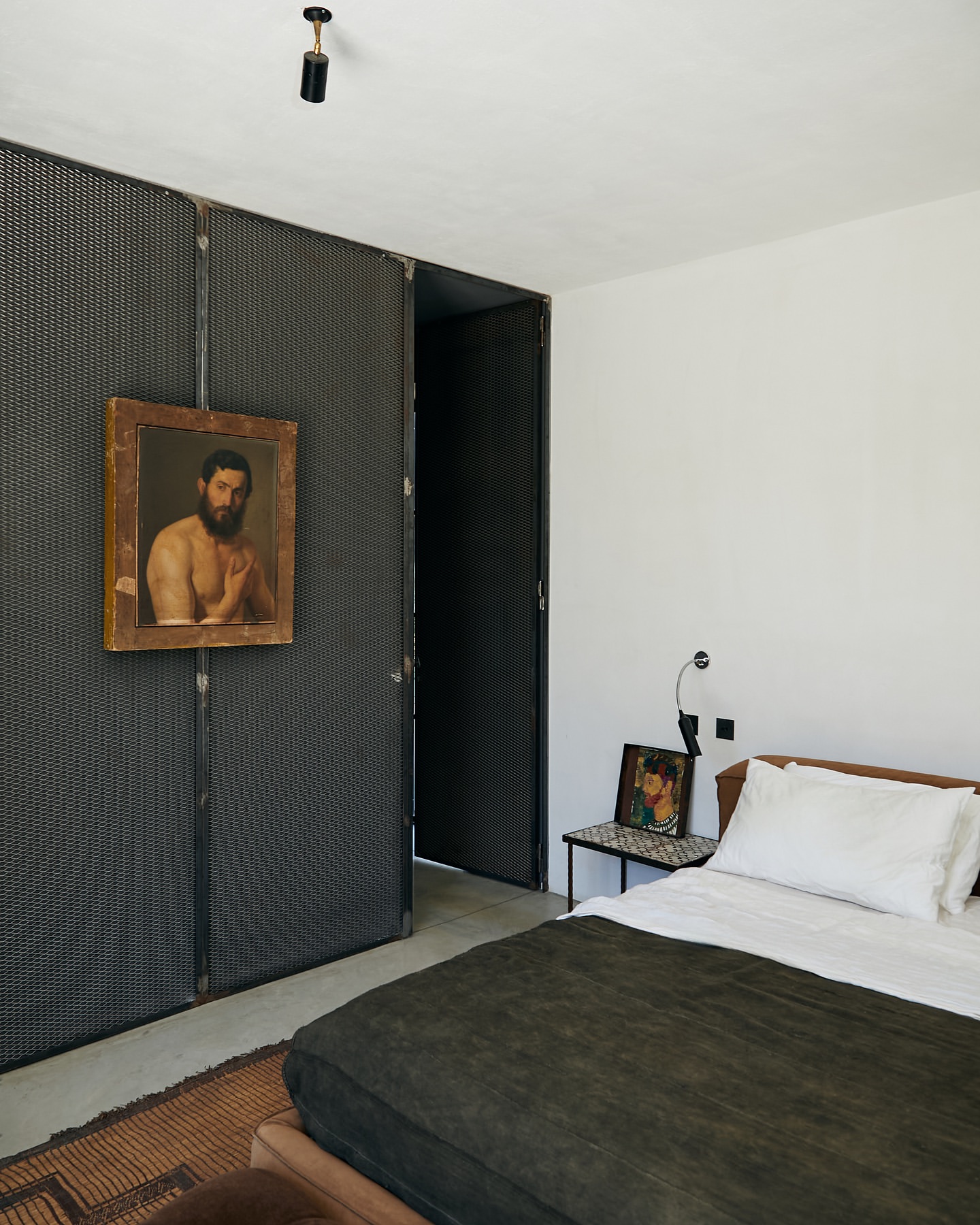 Interior bedroom view showcasing a bed with a dark green cover, a black metal divider with an art piece, and white walls.