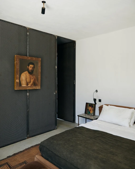 Interior bedroom view showcasing a bed with a dark green cover, a black metal divider with an art piece, and white walls.