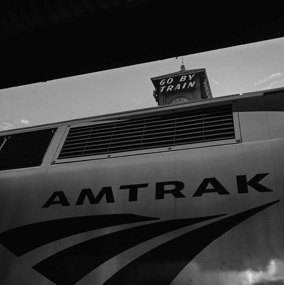 Black and white image of an Amtrak train with the words 'Go By Train' on a tower, promoting travel via train.