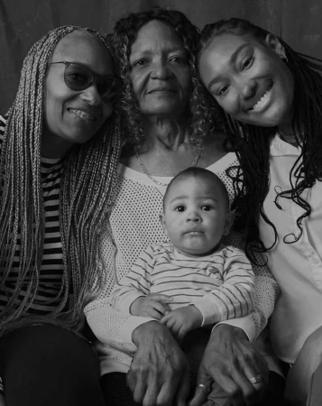 Four generations of African-American women pose together in a close-up studio portrait, including an infant held by an elderly woman.