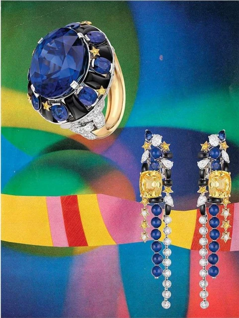 Close-up product shot of a gold statement ring with a large blue sapphire and matching dangling earrings on a colorful background.