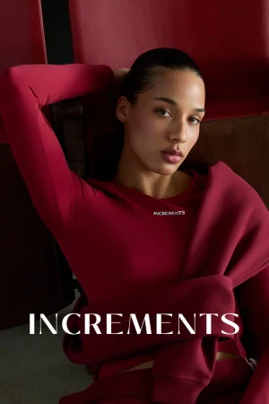 Woman in red long-sleeve top with hair tied back posing against a red theater seat background