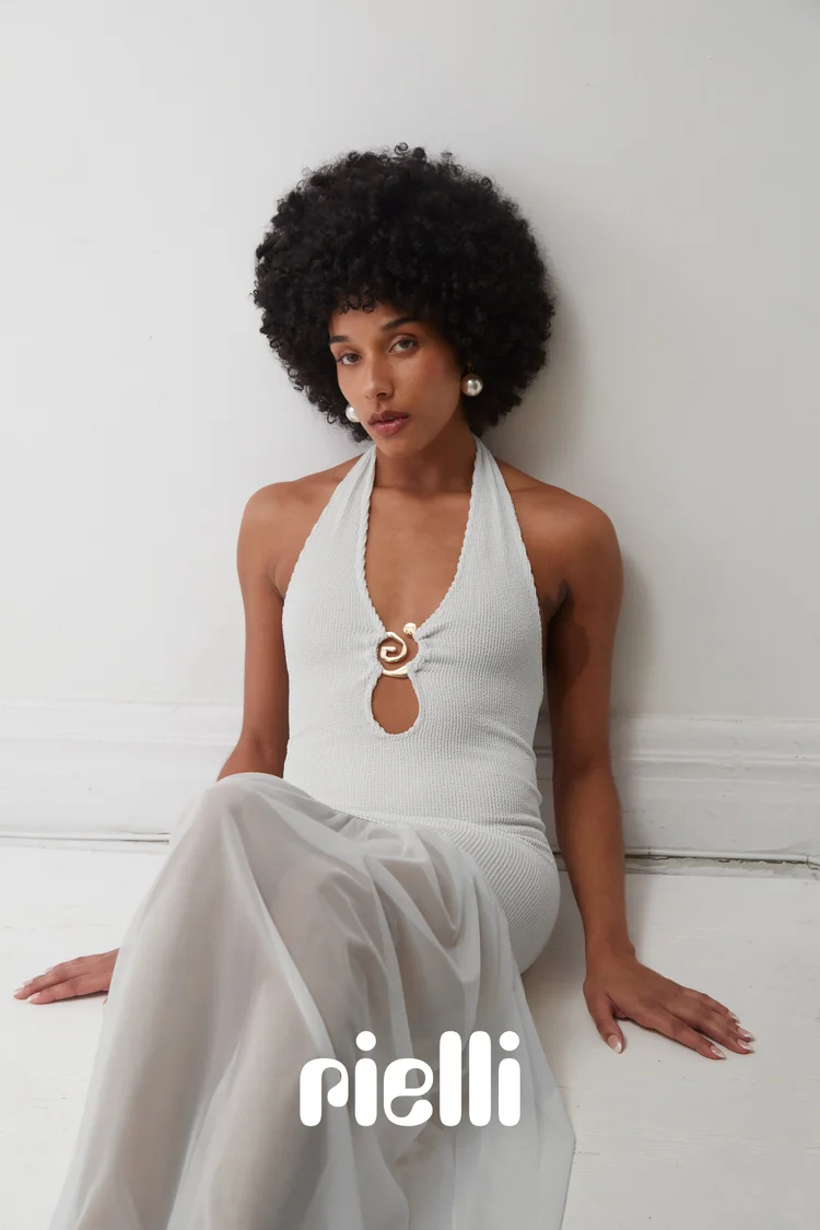 Woman with an afro hairstyle seated on the floor wearing a white halter dress with a gold clasp by photographer Elle Edwards