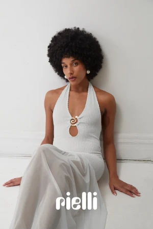 Woman with an afro hairstyle seated on the floor wearing a white halter dress with a gold clasp by photographer Elle Edwards