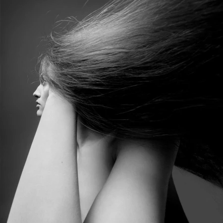 Black and white profile portrait of a woman with long hair streaming backward and arms raised near her face.