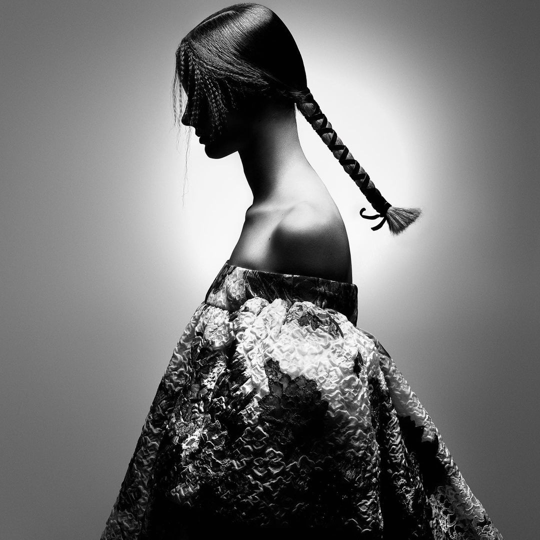 Monochrome portrait of a woman with styled hair in a braid wearing a textured dress, captured in a studio setting with soft lighting.