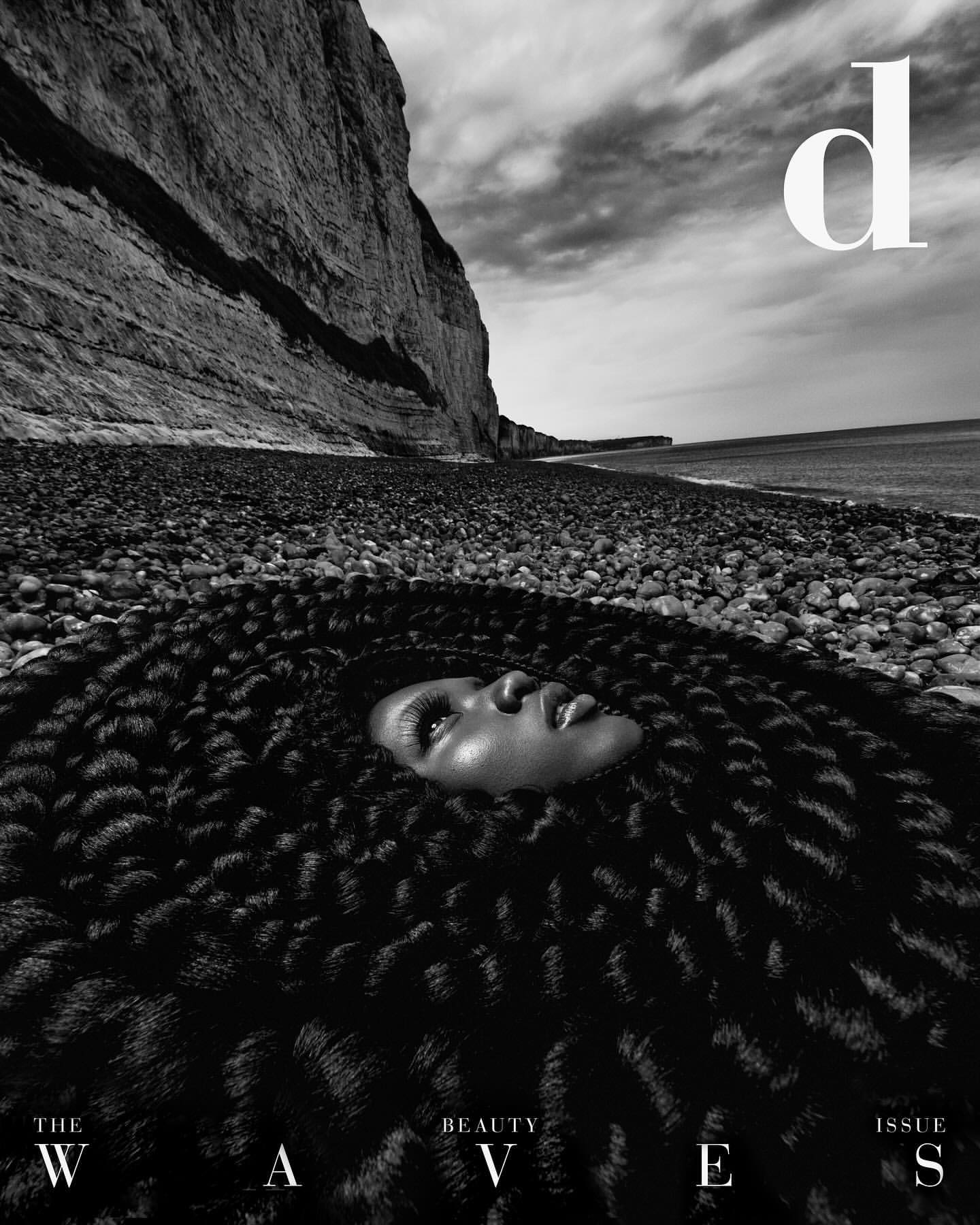 Black and white magazine cover shot of a person's face surrounded by a textured hair pattern against a rocky beach backdrop.