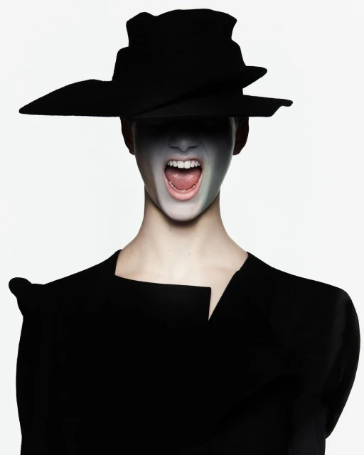 An adult female with face paint and wearing a sculptural hat and black garment in a studio setting with neutral backdrop.