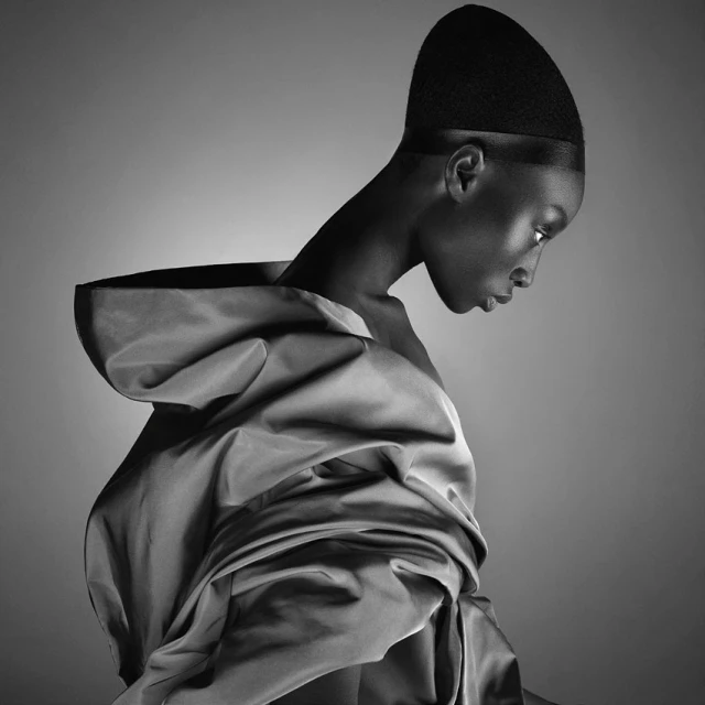 Black and white portrait of an African American woman wearing couture fashion with head covering and draped fabric against a gradient background.