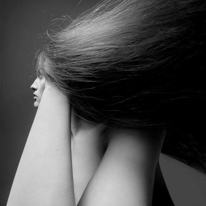 Black and white profile portrait of a woman with long hair streaming backward and arms raised near her face.