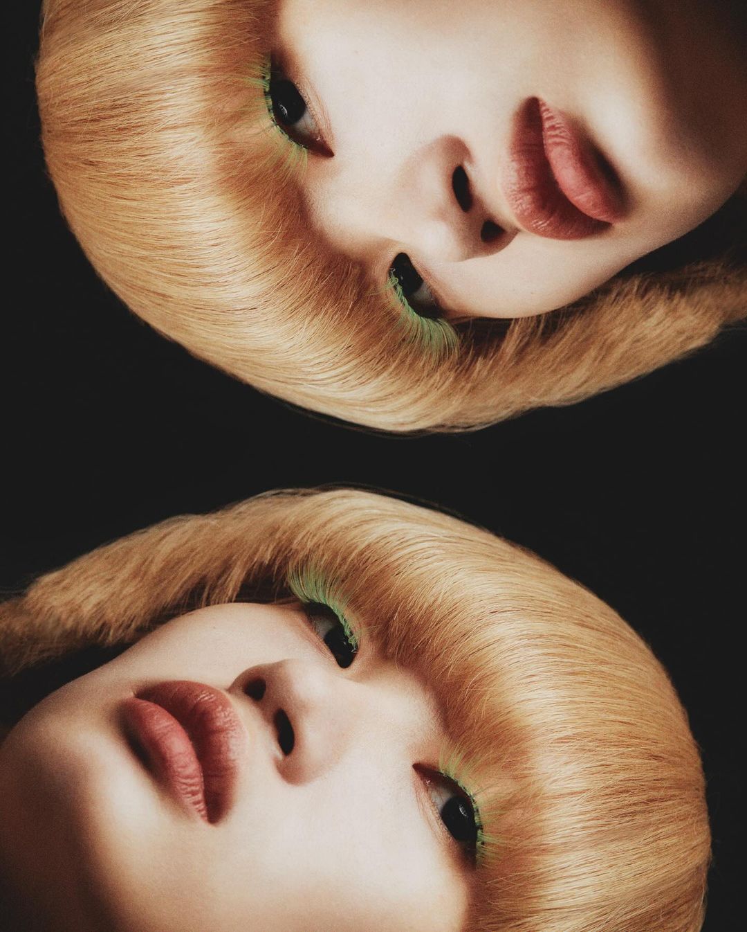 Close-up studio portrait of a woman with fair skin and blonde hair, featuring bright green eye makeup and striking red lipstick.