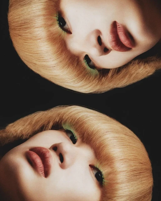 Close-up studio portrait of a woman with fair skin and blonde hair, featuring bright green eye makeup and striking red lipstick.
