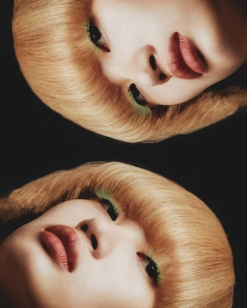 Close-up studio portrait of a woman with fair skin and blonde hair, featuring bright green eye makeup and striking red lipstick.