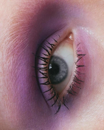 Close-up shot of a single eye with long eyelashes, pink and purple lighting, and smooth skin texture in a beauty-focused composition.