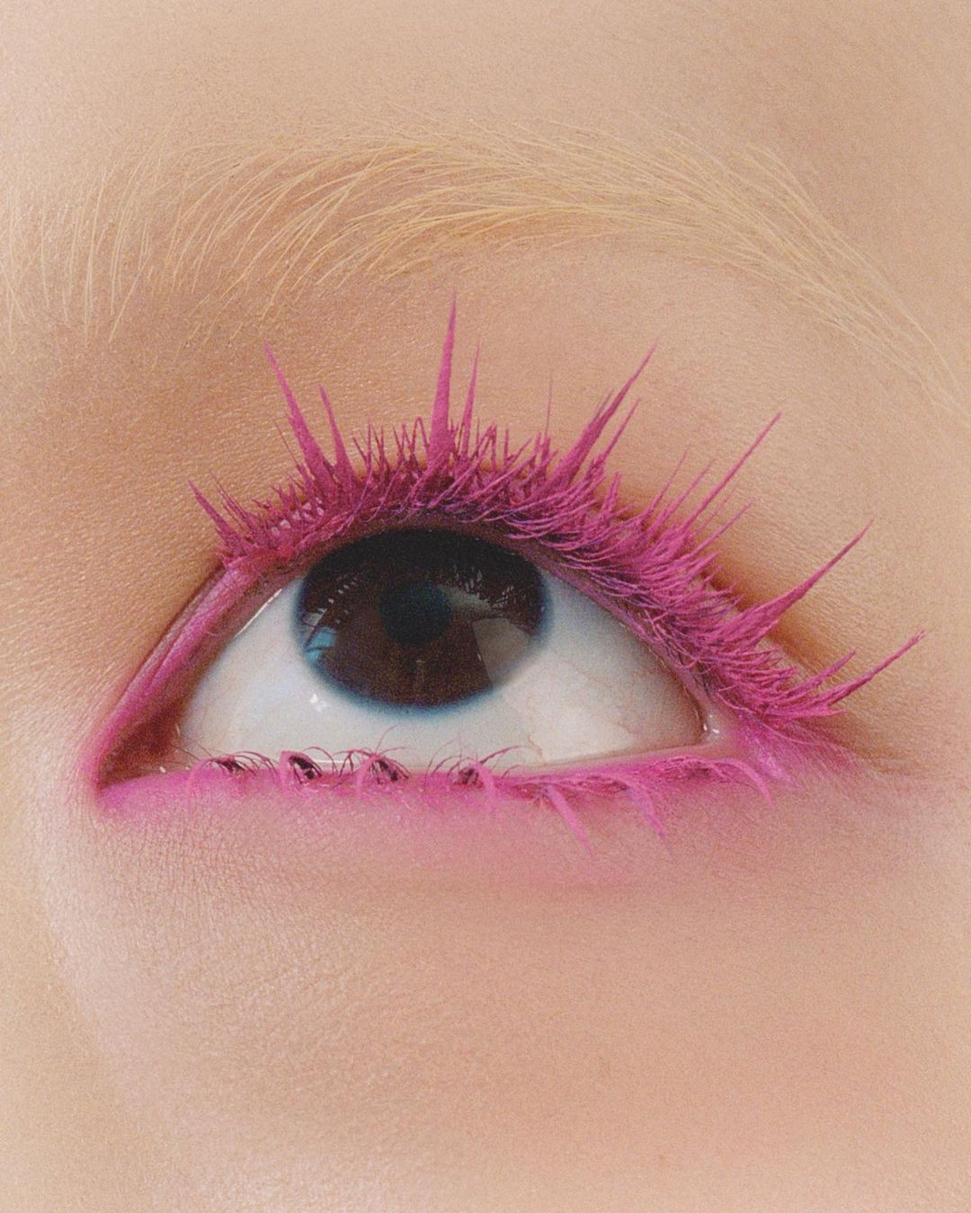 Close-up of a single eye with bright pink mascara and eyeliner, set against a light skin tone, creating a bold and striking beauty statement.