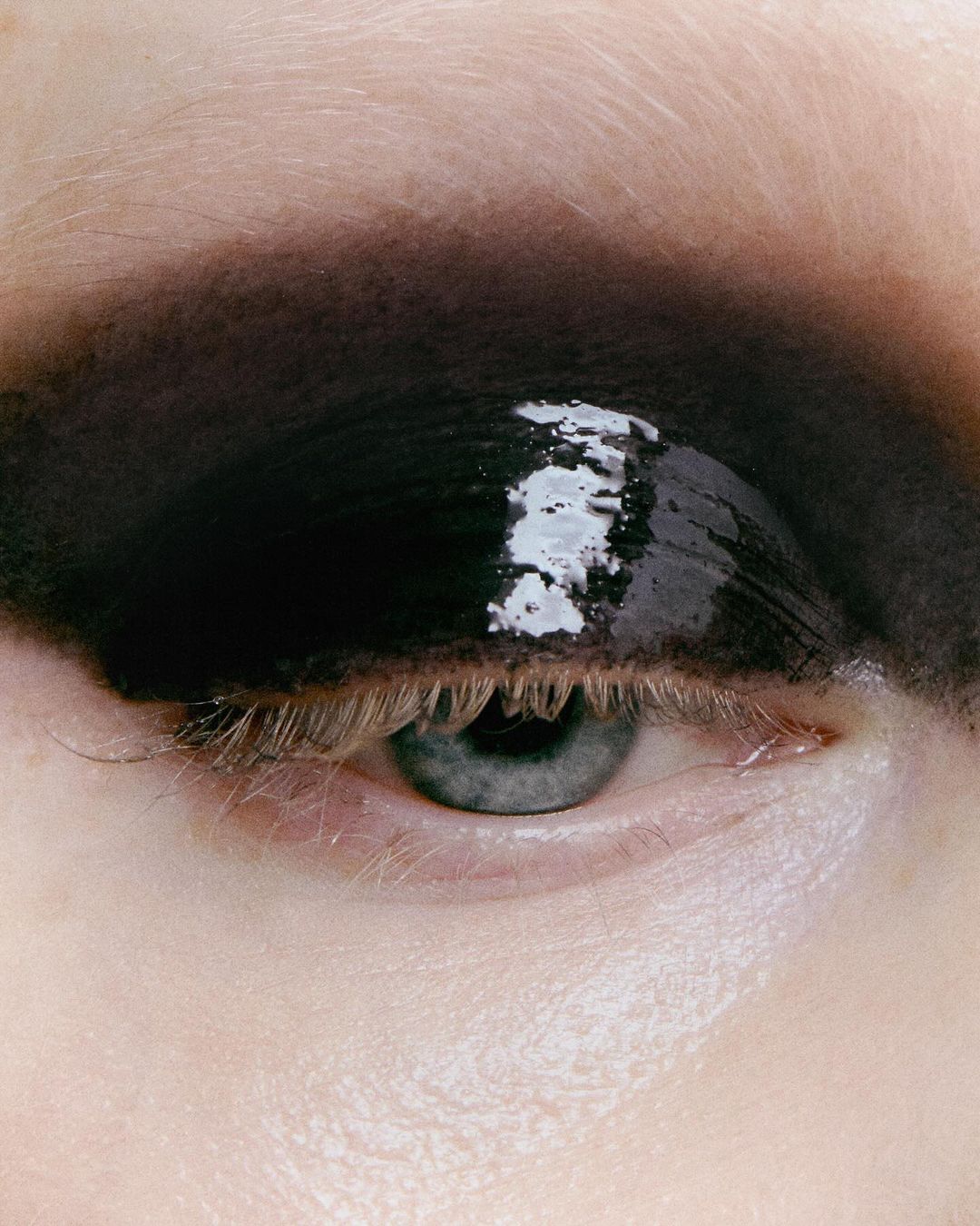 Close-up of an eye with heavy, glossy black eyeshadow extending to the eyebrow for a dramatic, beauty-focused, cosmetic presentation.