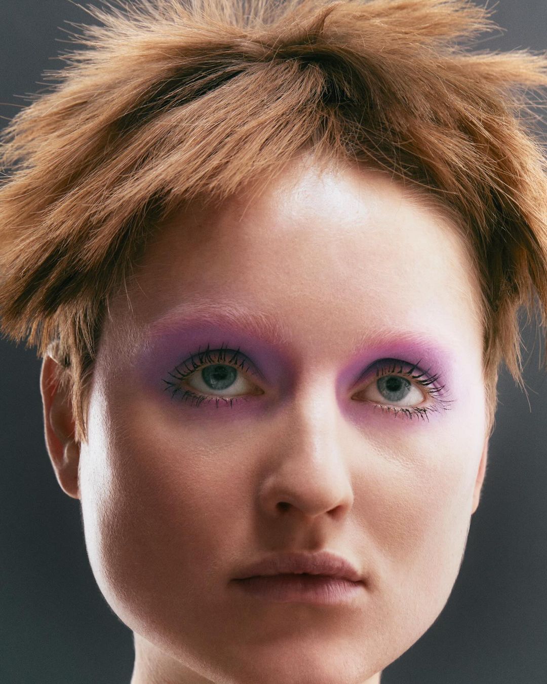 Close-up of a woman with short brown hair and purple eyeshadow. Beauty shot with focus on face and makeup, captured with a shallow depth of field.