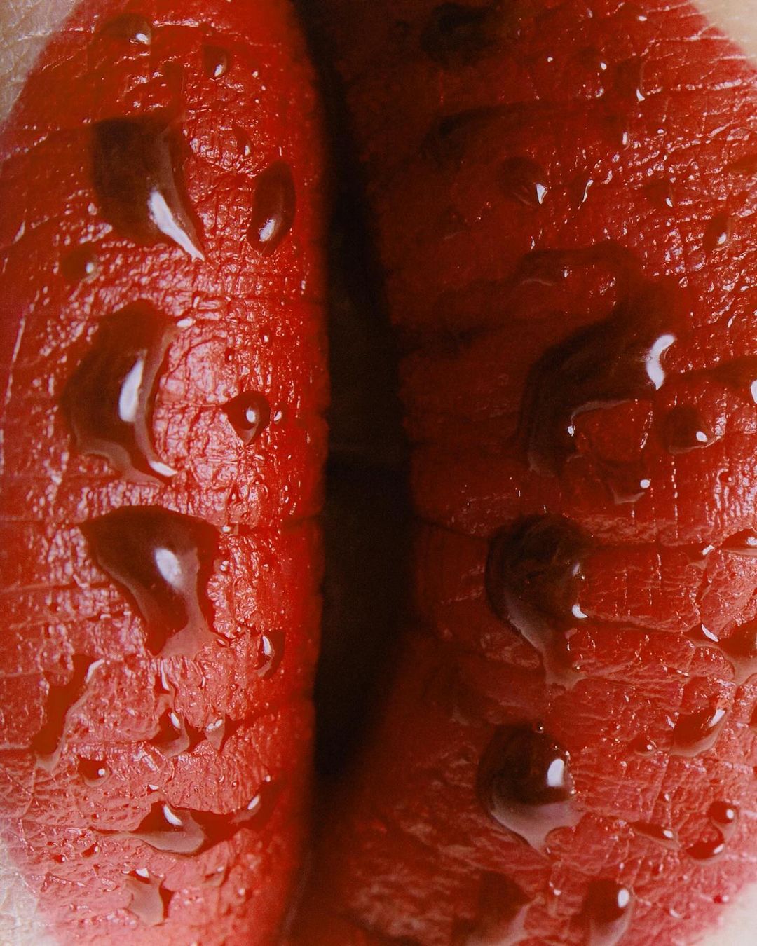 Close-up of glistening, bright red lips with water droplets emphasizing texture and vibrancy, creating a visually striking and sensual image.