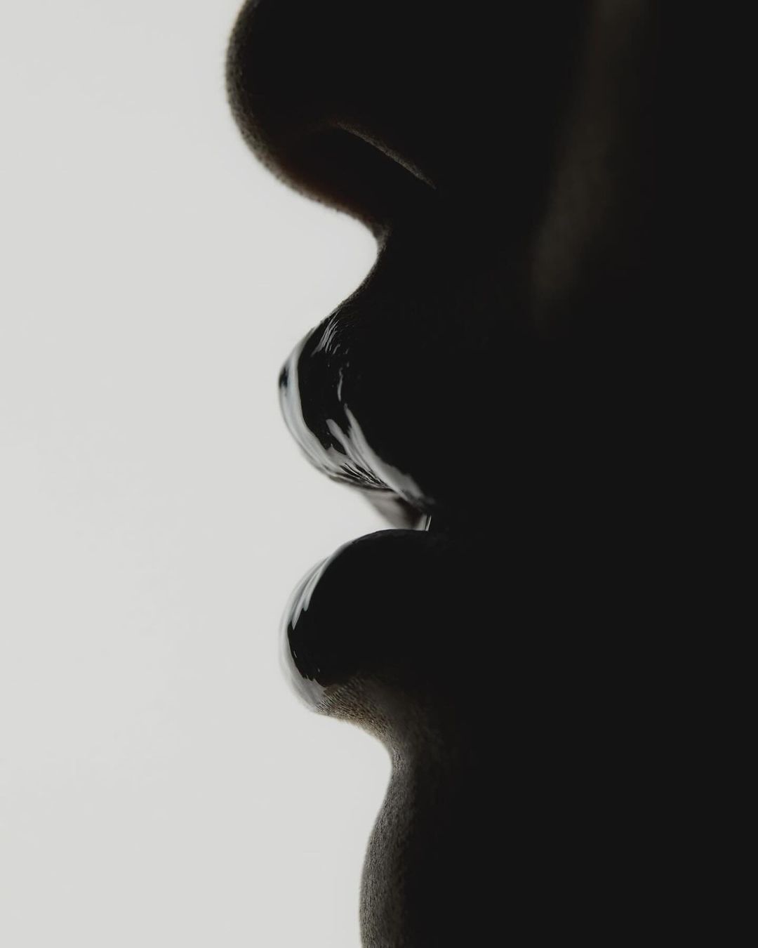 Striking monochrome close-up shows the silhouette of a person's face, featuring smooth skin and dramatic lighting against light background.