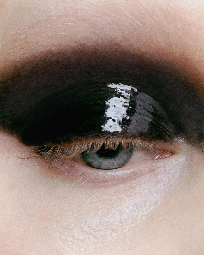 Close-up macro portrait of a blue eye with heavy glossy black eyeshadow and pale lashes photographed by Juliette Allix.
