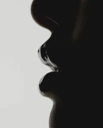 Extreme close up profile view of glossy lips in shadow against a bright white background by Juliette Allix