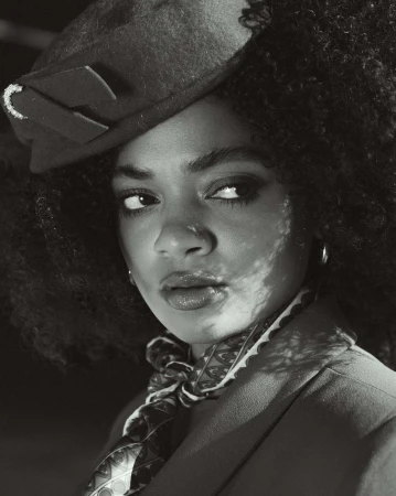 Close-up portrait of a Black woman in London wearing a patterned headscarf and hat by photographer Junior Butler.