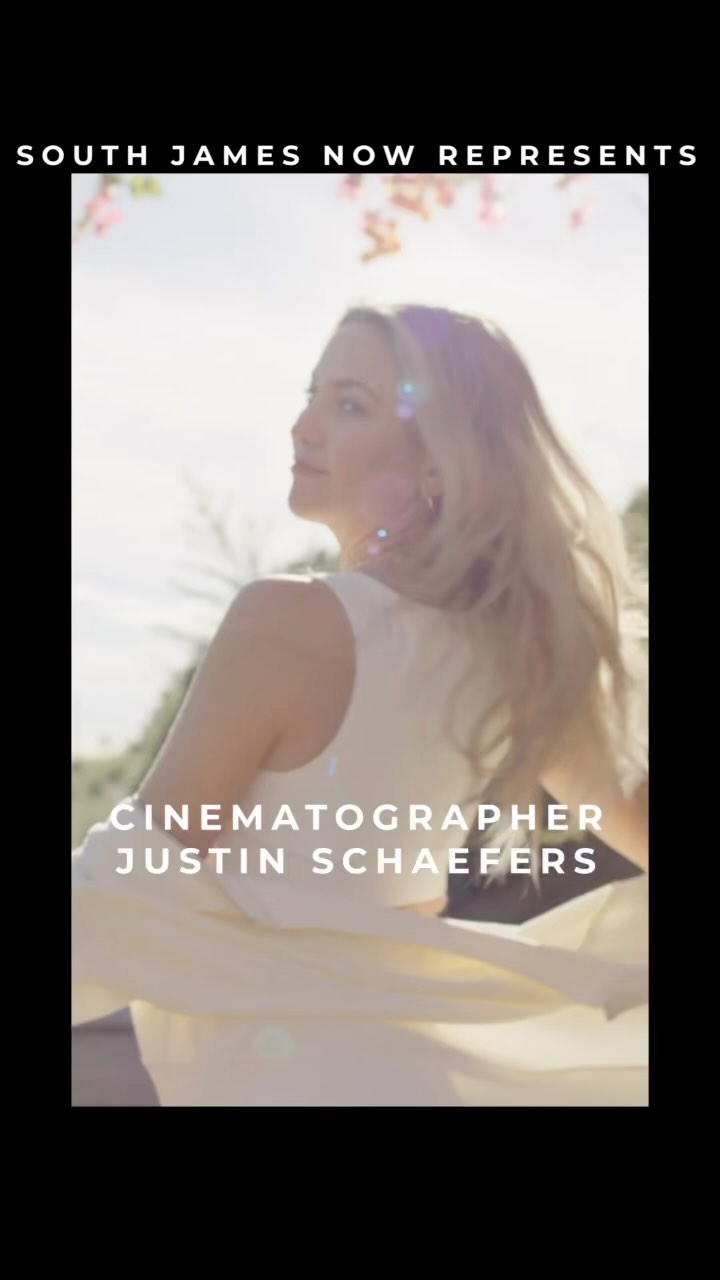 Portrait of an adult woman with long blonde hair wearing a white top and a white shawl outdoors in bright, sunny weather with greenery.