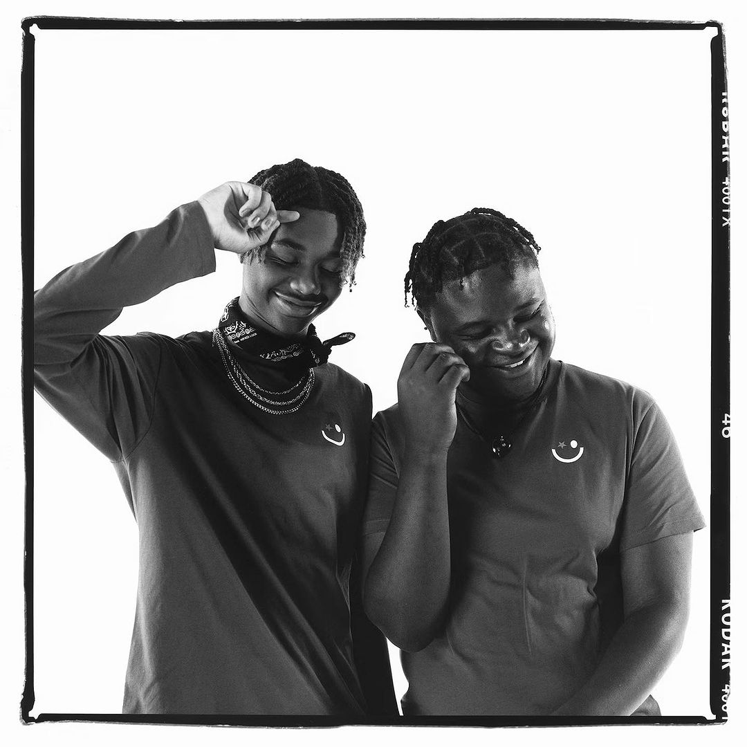 Black and white portrait of two smiling young African American men wearing t-shirts with smiley face logos in a photo studio.