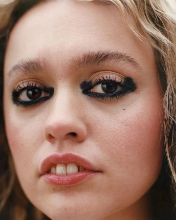 Close-up portrait of a young woman with heavy dark smudged eye makeup and wavy blonde hair.