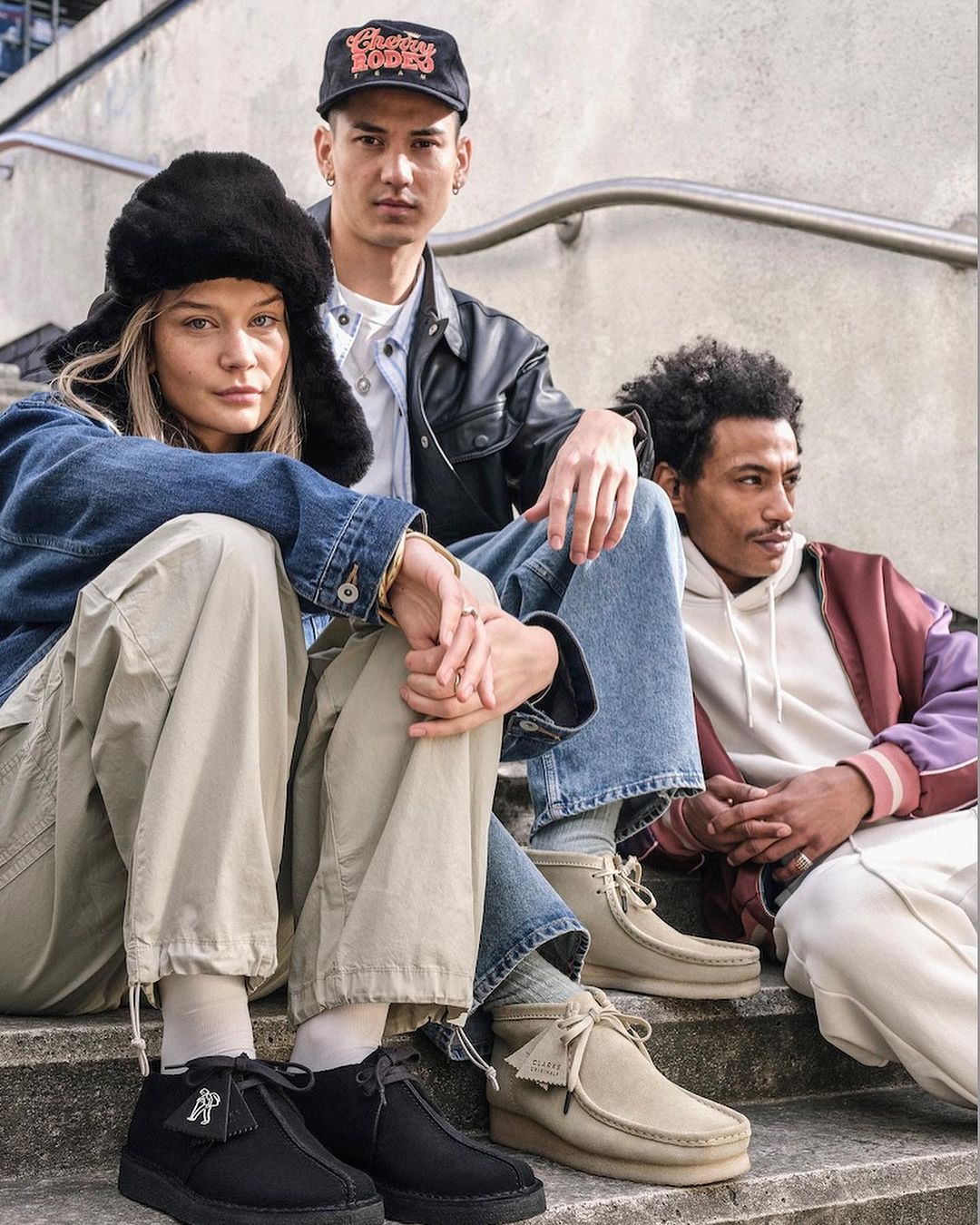 Three people are sitting on concrete steps wearing Clarks shoes and casual clothing, photographed at eye-level in an urban setting.