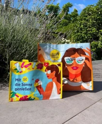 Two colorful shopping tote bags featuring illustrated summer beach scenes by illustrator Kaja Merle outdoors.