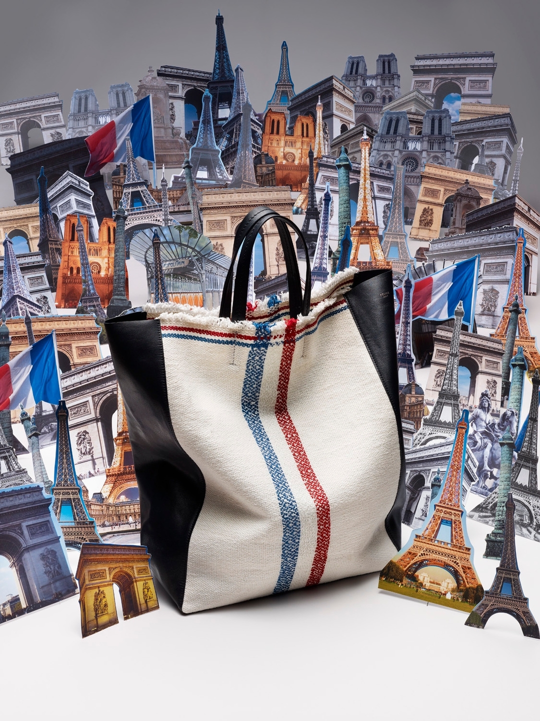 Fashion still life of a textile tote bag with black leather trim, against a backdrop of Eiffel Tower and Arc de Triomphe illustrations.