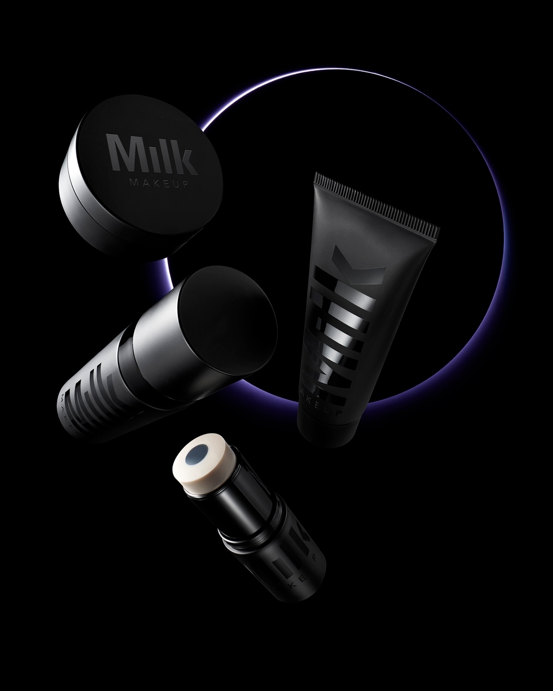 Still life shot of Milk Makeup brand products in various cylindrical containers set against a dark backdrop with a purple glowing circle.