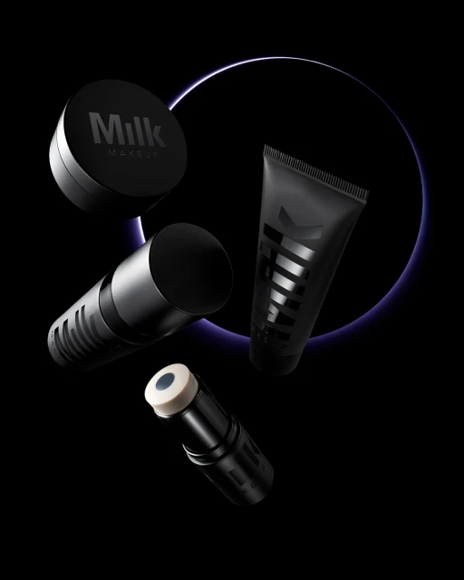 Still life shot of Milk Makeup brand products in various cylindrical containers set against a dark backdrop with a purple glowing circle.