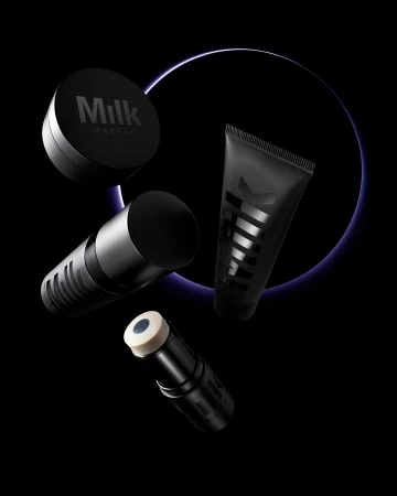 Still life shot of Milk Makeup brand products in various cylindrical containers set against a dark backdrop with a purple glowing circle.