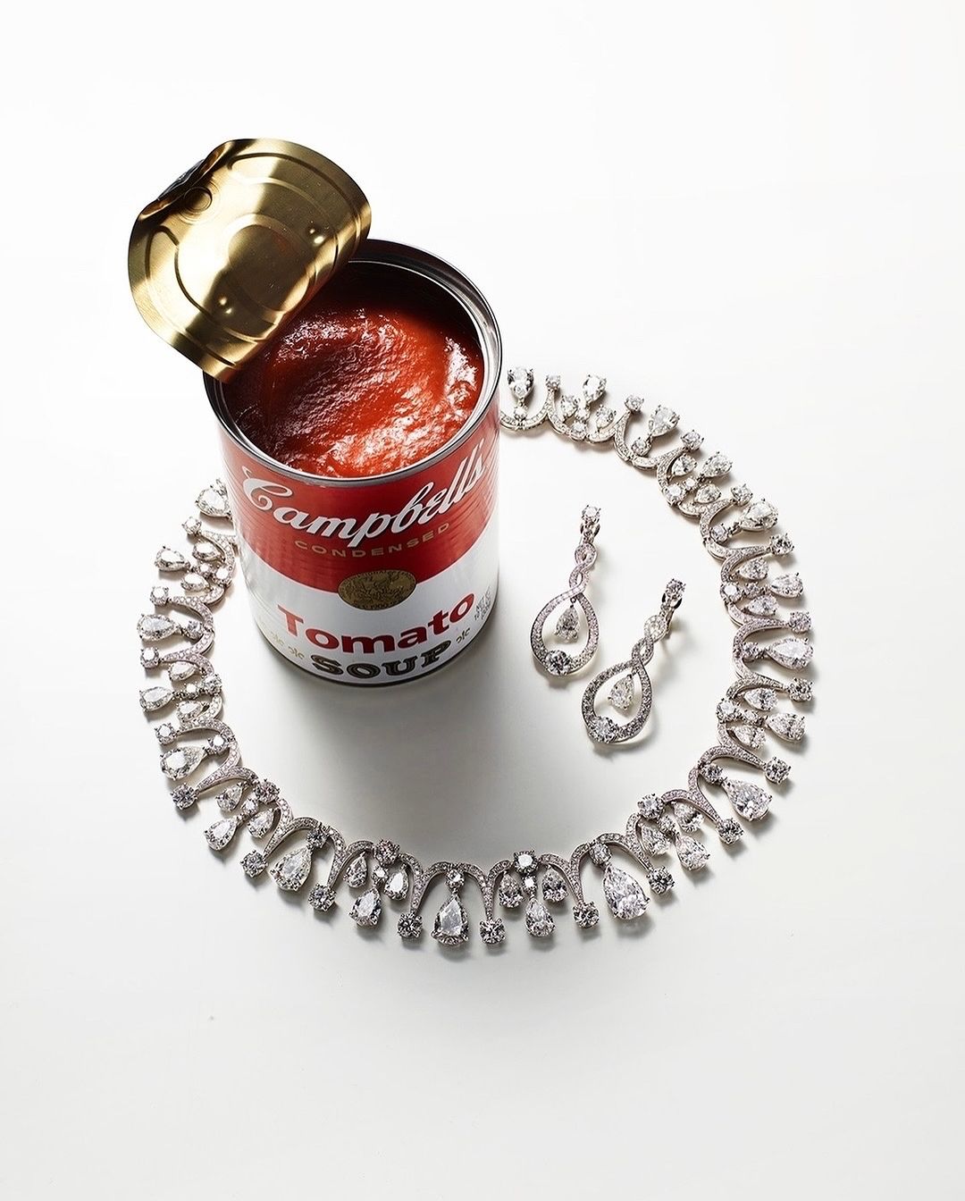 Silver diamond necklace and earrings displayed with a can of Campbell's Tomato Soup on a white background, studio lighting.