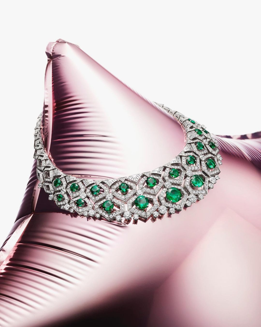 Emerald and diamond necklace displayed on a pink metallic surface. High-end jewelry and gemstone, fine craftsmanship.
