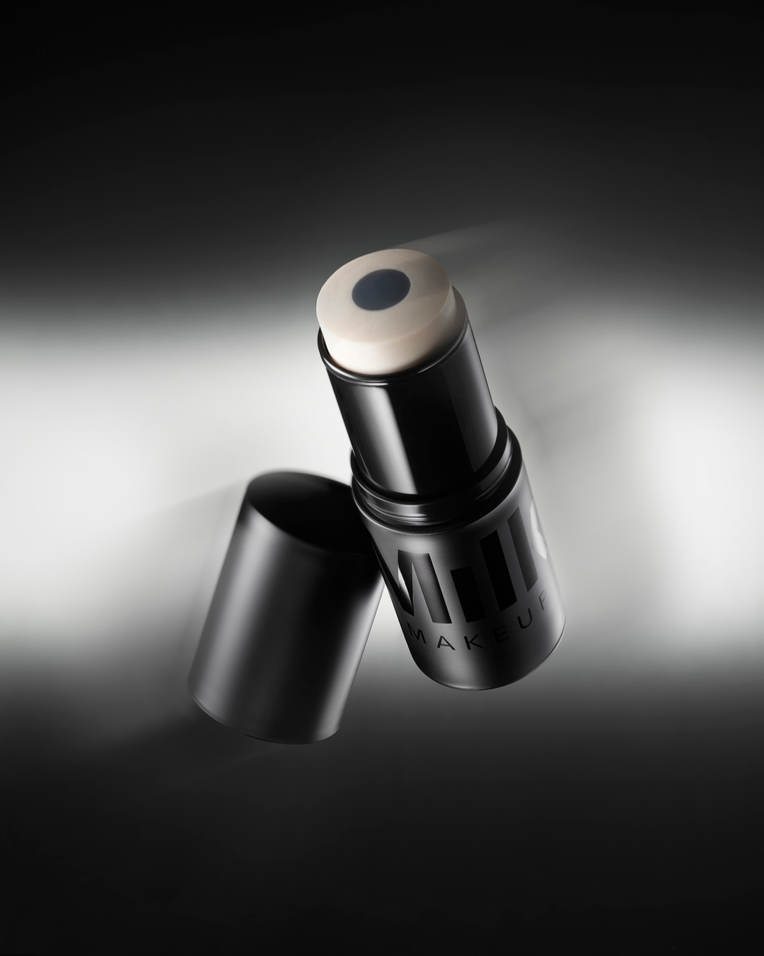 Close-up of a black Milk Makeup product stick and cap against a gradient gray background, showcasing beauty product for cosmetic use.