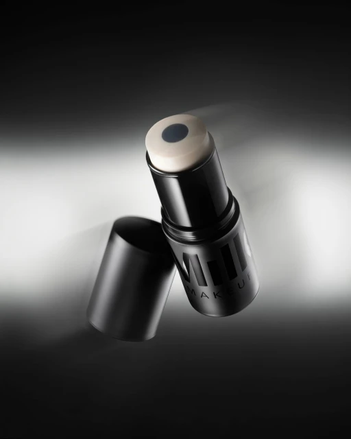 Close-up of a black Milk Makeup product stick and cap against a gradient gray background, showcasing beauty product for cosmetic use.