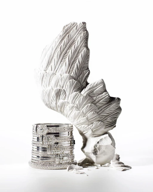 Jewelry still life featuring stacked bracelets and a sculptural white wing, presented against a bright white backdrop in a studio setting.