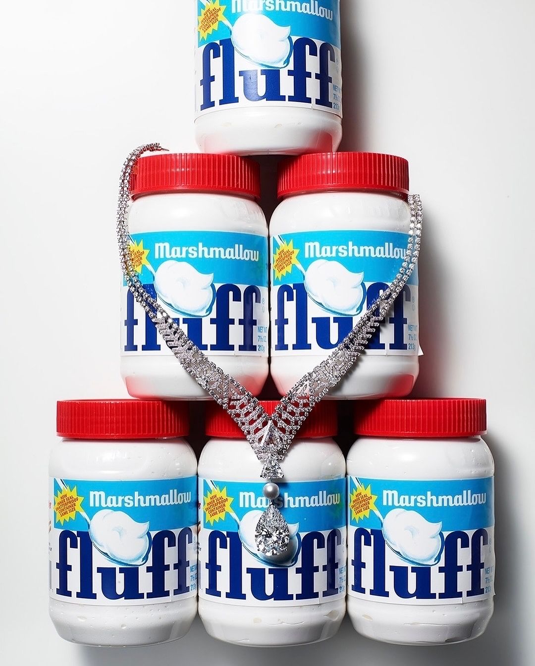 Diamond necklace draped over stacked Marshmallow Fluff jars against a white background in a studio shot promoting confectionary and jewelry.