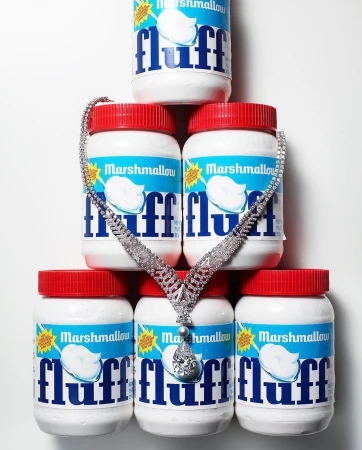 Diamond necklace draped over stacked Marshmallow Fluff jars against a white background in a studio shot promoting confectionary and jewelry.