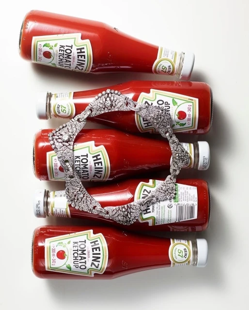 Overhead shot: Five Heinz tomato ketchup bottles, caps at alternating ends, with a diamond headband draped across the middle three.