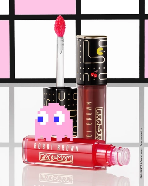 Bobbi Brown Pac-Man lip gloss in red and black packaging, featuring a pink Pac-Man ghost, against a patterned background.