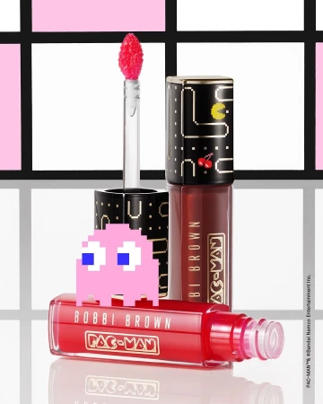 Bobbi Brown Pac-Man lip gloss in red and black packaging, featuring a pink Pac-Man ghost, against a patterned background.