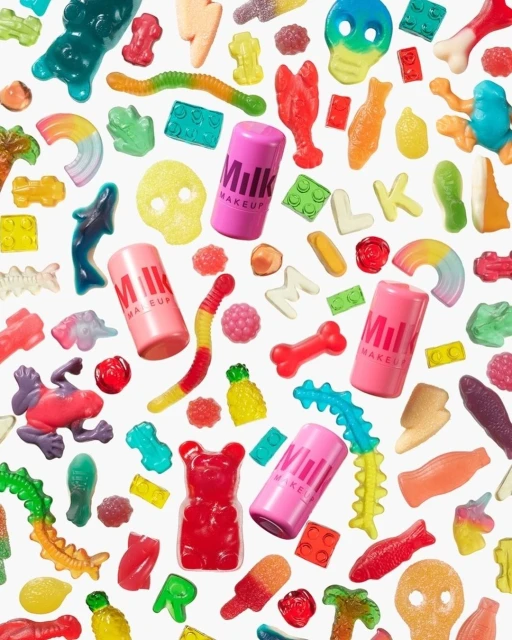Overhead shot of gummy candies and Milk Makeup tubes on a white background. Colorful treats and beauty products create a playful scene.