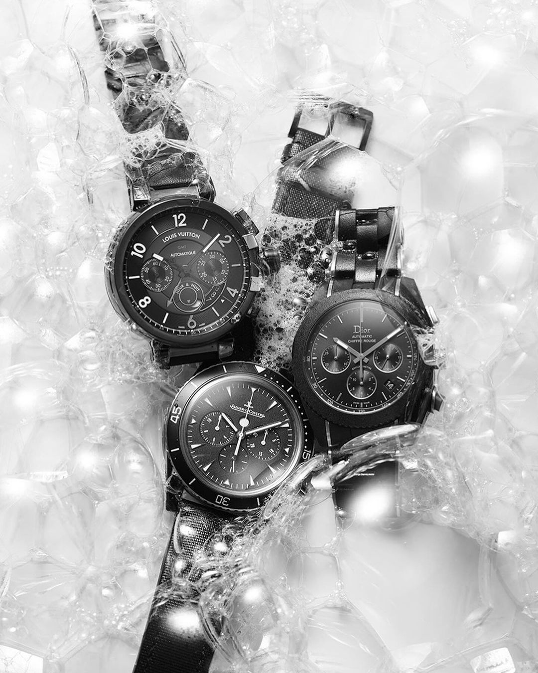Three luxury wristwatches, Louis Vuitton and Dior brands, set against a backdrop of transparent spheres, creating a modern, monochrome still life.